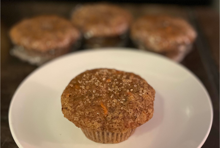 A carrot cake muffin sprinkled with raw sugar is centered on a white plate.