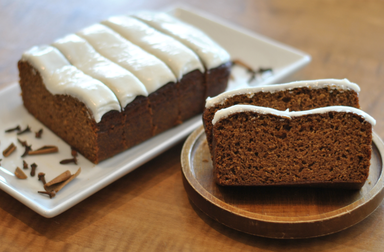 Two plates feature slices of iced gingerbread loaf and a blend of seasonal spices strewn about. 